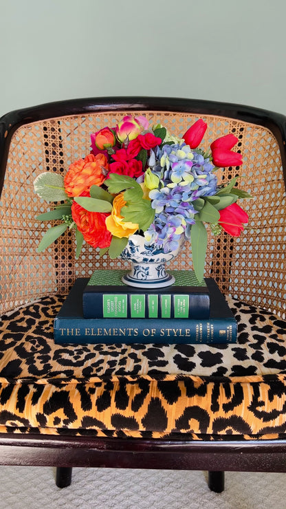 A bright, beautiful faux floral arrangement in a blue and white footed bowl. 